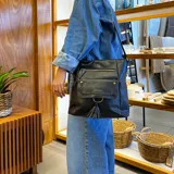 Bandolera negra de cuero sintético con cierre superior y correa larga regulable. Tiene bolsillo frontal con tapa y broches magnéticos, detalle de trenza artesanal, división interna, bolsillos internos y bolsillos laterales tipo ojal.