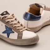 Zapatillas bajas de cuero vacuno color blanco, con estrella azul metalizada en el lateral, detalles en gamuza color aluminio y contrafuerte azul metalizado.