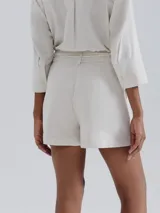 Short de lino en color crudo, de corte recto y tiro medio. Presenta una cintura con pasacintos y un cordón trenzado decorativo con borlas en el frente.