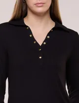Remera negra de tejido de punto acanalado, de silueta al cuerpo, con cuello polo, abertura frontal en V con botones dorados, mangas largas ajustadas con puños abotonados y ruedo recto.