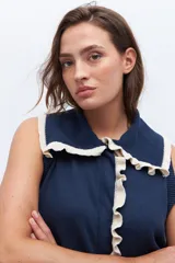 Chaleco de punto sin mangas, color azul marino, con cuello y frente adornados con volados en contraste de color blanco o crudo.