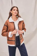 Campera marrón de gamuza sintética con cuello, puños y ruedo de piel sintética blanca. Presenta cierre frontal con cremallera, bolsillos laterales y detalles en cuero sintético negro.