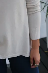 Sweater de tejido de punto en color beige, con cuello redondo, mangas tres cuartos y corte holgado con ruedo ligeramente más largo en la parte posterior.