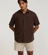 Camisa de corte relajado para hombre, confeccionada en una mezcla de cáñamo y algodón. Presenta cuello inglés, manga corta, cierre frontal con botones y un bolsillo en el pecho con una pequeña etiqueta aplicada.