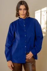 Camisa de pana azul con cuello alto tipo mao con volados, cierre frontal con botones y mangas largas abullonadas.