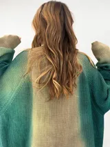 Buzo tejido de lana merino con diseño oversize, manga ranglan y cuello levemente elevado. Presenta un efecto de teñido degradado que combina tonos verdes y beige.