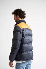 Campera puffer de nylon para hombre, con diseño bicolor en azul marino y mostaza en la parte superior. Cuenta con cierre frontal completo, mangas largas con puños elásticos y bolsillos laterales con cierre. Incluye logo estampado en el pecho.