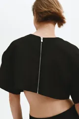 Cropped top negro con leve brillo, de manga corta, escote redondo, hombros caídos y cierre visible en la espalda.