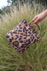 Cartera mini tipo tote bag con estampado animal print de leopardo en tonos marrones y negros. Tiene manijas rígidas metálicas color bronce.
