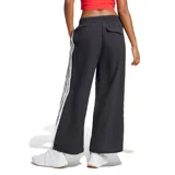 Pantalón de corte ancho y estilo urbano, confeccionado en tejido liviano color negro. Presenta cintura elástica con cordón ajustable, bolsillos laterales y las icónicas tres tiras de la marca en los costados, junto con el logo de Adidas bordado en la pierna.