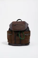 Mochila de estructura blanda confeccionada en nylon color marrón con estampado de cuadros tipo tartán. Presenta bolsillos laterales con cierre, solapa superior con bolsillo frontal y un detalle de cordón elástico en color verde neón.