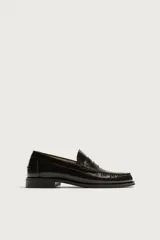 Mocasines de vestir tipo loafer para hombre, confeccionados en cuero marrón oscuro con acabado brillante. Presentan diseño clásico de antifaz en el empeine, costuras visibles en relieve y suela plana con un ligero tacón.