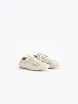 Zapatillas urbanas de cuero vacuno en color beige, con detalles de volados en los laterales de los cordones y suela de goma plana con textura.