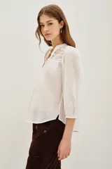 Camisa de algodón color celeste, con cuello mao, cierre frontal parcial con botones y detalles de encaje en los hombros y canesú. Presenta mangas largas abullonadas con puños elásticos.