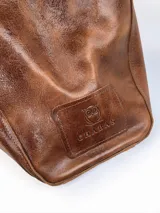 Bolso tipo tote grande de cuero genuino marrón, con asas de hombro dobles, bolsillo exterior con botón a presión y llavero colgante con la marca grabada.