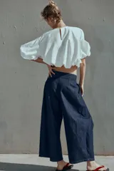 Pantalón tipo culotte de tiro alto confeccionado en denim azul oscuro. Presenta pinzas delanteras, pernera ancha y corta, bolsillos laterales ocultos y cierre frontal con cremallera, botón y ganchos.