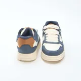 Zapatillas urbanas de diseño tricolor en tonos azul marino, crema y detalles en marrón. Presentan una silueta clásica con cordones gruesos y suela de goma con textura dentada.