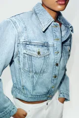Cazadora corta de denim color celeste con cuello solapa, manga larga y hombreras. Cuenta con bolsillos delanteros con solapa y cierre frontal de botones metálicos.