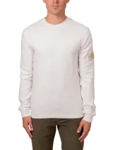 Remera blanca de manga larga con cuello redondo y puños de canalé. Tiene un parche con el logo de Calvin Klein en la manga.