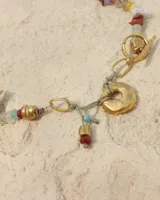 Collar corto de estilo artesanal, compuesto por una variedad de piedras naturales en tonos tierra, verdes, rojos y amarillos, intercaladas con pequeñas perlas de río. Presenta dijes de bronce macizo con formas orgánicas, incluyendo una figura de pez y un dije circular central, unidos por un cierre de barra y argolla.