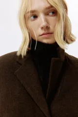 Blazer de botonadura sencilla en tejido afieltrado color marrón oscuro. Presenta solapas de muesca, hombreras, cierre frontal de tres botones y dos bolsillos delanteros de parche. El diseño es forrado y de corte estructurado.