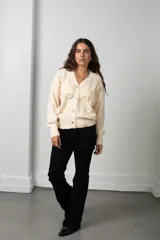 Saco de punto color manteca con cuello en V, cierre frontal de botones y apliques de flores bordadas en relieve. Presenta diseño de trenzas y puños acanalados.