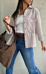 Camisa clásica a rayas verticales blancas y tostadas, con botones marrones y bordado floral en el frente.