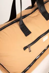Bolso de gran capacidad color beige, con asas fijas superiores y correa de cinta negra desmontable y regulable. Presenta un bolsillo externo con cierre, un compartimento inferior con cierre y logo de la marca Daniel Cassin en el frente.