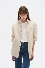 Campera marrón de manga larga confeccionada en algodón, con cuello camisero, cierre frontal con botones a presión y puños elásticos fruncidos.