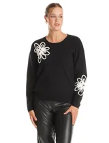 Buzo tejido color negro con cuello a la base y mangas largas. Presenta un diseño floral en relieve en color blanco ubicado en la parte superior delantera y en la parte inferior de una de las mangas.