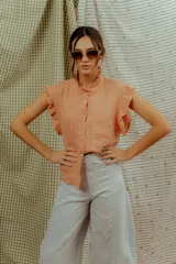 Blusa color salmón de lino, con mangas sin mangas adornadas con volados, cuello mao con detalle de ruches y cierre frontal de botones.