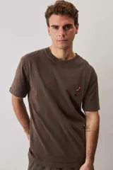 Remera de calce relajado y cuello redondo, color verde musgo con efecto lavado, y pequeño bordado de un morrón en el pecho.