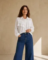 Camisa blanca de manga larga con cuello camisero, cierre frontal de botones y detalles de volados con bordado broderie en el frente.