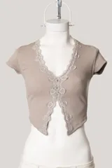 Remera de tejido acanalado color beige, con escote en V profundo decorado con puntilla de encaje en los bordes, mangas cortas y diseño abierto en el frente.