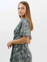 Vestido largo de fiesta con diseño cruzado, escote en V y drapeado lateral en la cintura. Presenta mangas cortas acampanadas y falda amplia con caída fluida. Confeccionado en tejido liviano con acabado plisado y estampado floral metalizado.