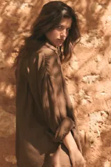 Camisa oversize marrón de gasa, con cuello solapa, manga larga de hombro caído con puño ancho, bolsillo aplicado en el frente y cierre frontal con botones.