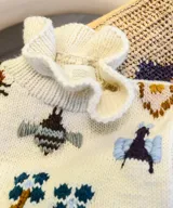 Chaleco de punto color marfil, con cuello alto estilo gorguera y bordados artesanales de insectos y elementos de la naturaleza en la parte delantera.
