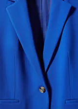 Blazer negro entallado de punto roma con solapas de muesca, hombros estructurados, abertura posterior y dos bolsillos de ribete delanteros.