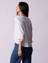 Blusa blanca de algodón marca Dash, con escote en V, abertura con botones, mangas 3/4 regulables con presilla y botón, y terminación de ruedo anudado.