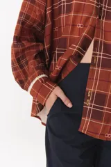 Camisa de corte holgado en color bordó con estampado de cuadros y monograma. Presenta cuello redondo con borde de puntilla, bolsillo frontal con detalle de puntilla, cierre frontal con botones y puños con terminación en puntilla.