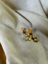 Par de aros colgantes con base circular color durazno y flores color crema con centro dorado.