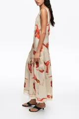 Vestido midi con vuelo en el bajo, de corte recto con tirantes anchos y escote cuadrado, confeccionado en mezcla de lyocell. Presenta un estampado artístico integral con figuras humanas en tonos rojos y naranjas sobre fondo crudo, además de costuras visibles decorativas.