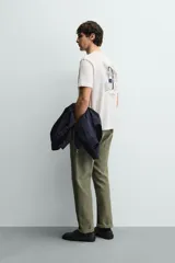 Camiseta de corte relajado, color blanco, con cuello redondo y manga corta. Presenta un pequeño estampado en el pecho con texto y un diseño gráfico más grande en la espalda.