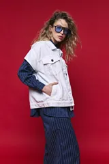 Chaleco de jean color blanco, de corte oversized, con cuello camisero, bolsillos delanteros con solapa y cierre frontal por botones metálicos.