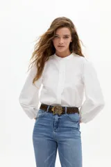 Camisa de algodón con estampado de rayas verticales en tonos azul y blanco. Presenta cuello mao, cierre frontal oculto con detalle de volado lateral y mangas abullonadas con puños elásticos.