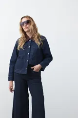 Campera de jean color negro con cuello de pana en tono marrón, cierre frontal con botones metálicos y bolsillos frontales tipo cargo.