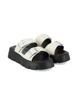 Sandalia de cuero graneado color blanco off-white, con suela chunky negra de poliuretano y doble tira ajustable con hebillas metálicas.