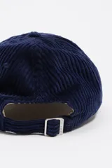 Gorra de béisbol confeccionada en pana, con diseño bicolor que combina una corona azul marino y una visera verde oscuro. Presenta un bordado tonal en el frente y ojales de ventilación.