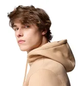 Buzo tipo canguro Columbia, color beige, con capucha ajustable mediante cordones, bolsillo frontal tipo canguro, puños y dobladillo acanalados. Presenta un pequeño parche con el logo de la marca en el pecho.