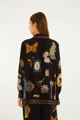 Blusa negra de viscosa con mangas largas y puños ajustables, escote en V con lazos frontales y silueta fluida, con estampado artístico de marcos, animales y elementos marinos.